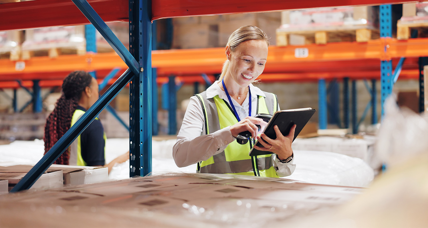 Warehouse manager using tablet to monitor intrusion detection system in Central Florida distribution center with safety vest and organized inventory shelving